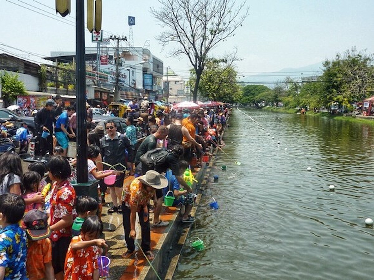 Hundreds of people gather around a moat.