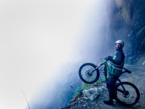 A cyclist raises his front wheel over a misty cliff in Yungas Road, Bolivia