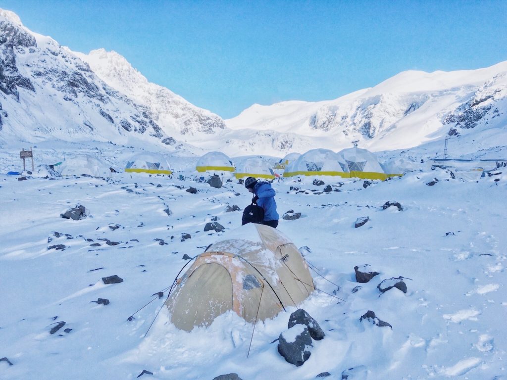 A mountain climber sorts his bag outside his tent in the snow