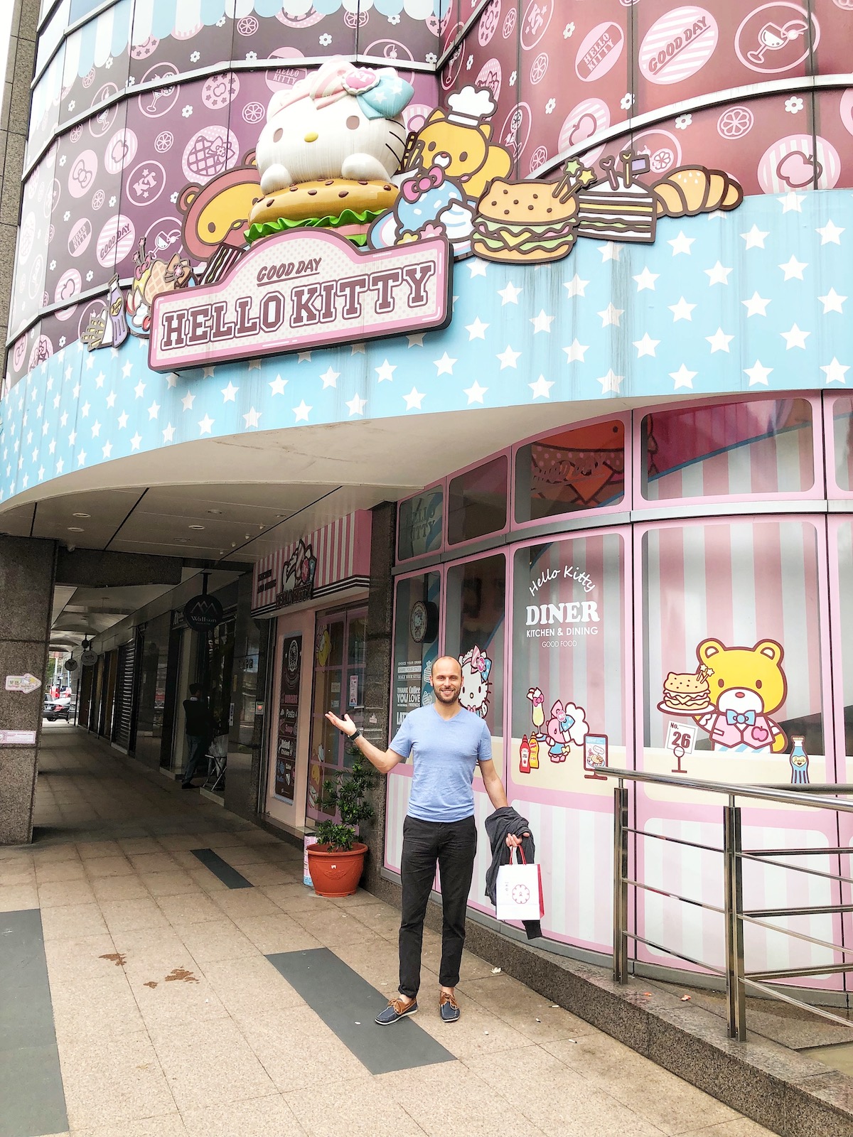 A man in blue smiles and poses outside a pink Hello Kitty restaurant in Taipei, Taiwan