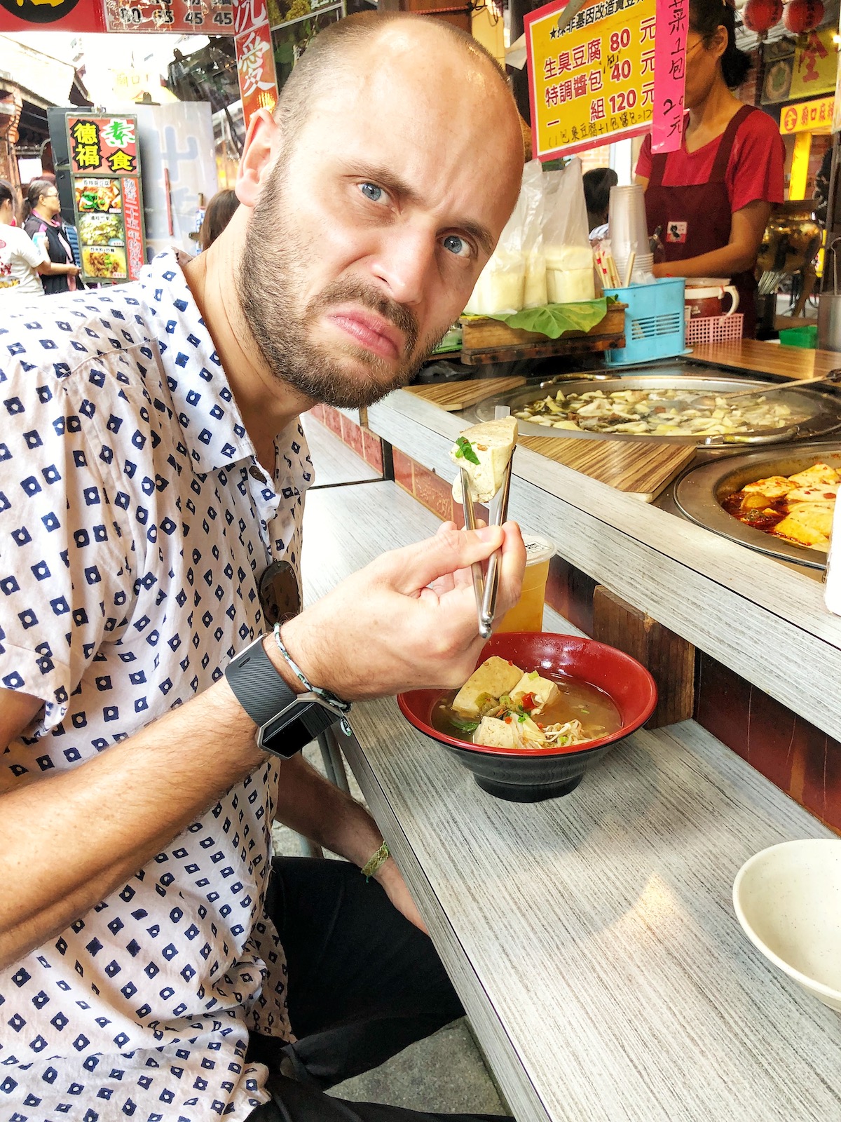 A man pulling a disgusted face eating stinky tofu in Taipei, Taiwan