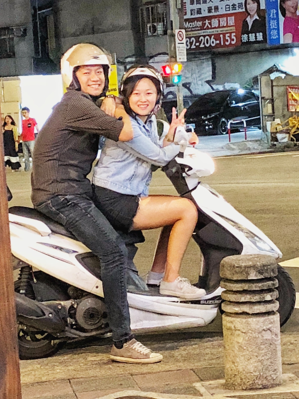 An Asian man and woman smile on a white scooter