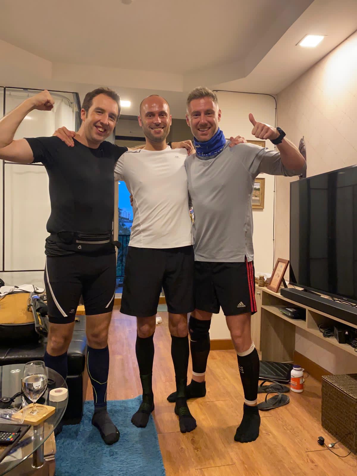 3 men in running gear posing in a small living room