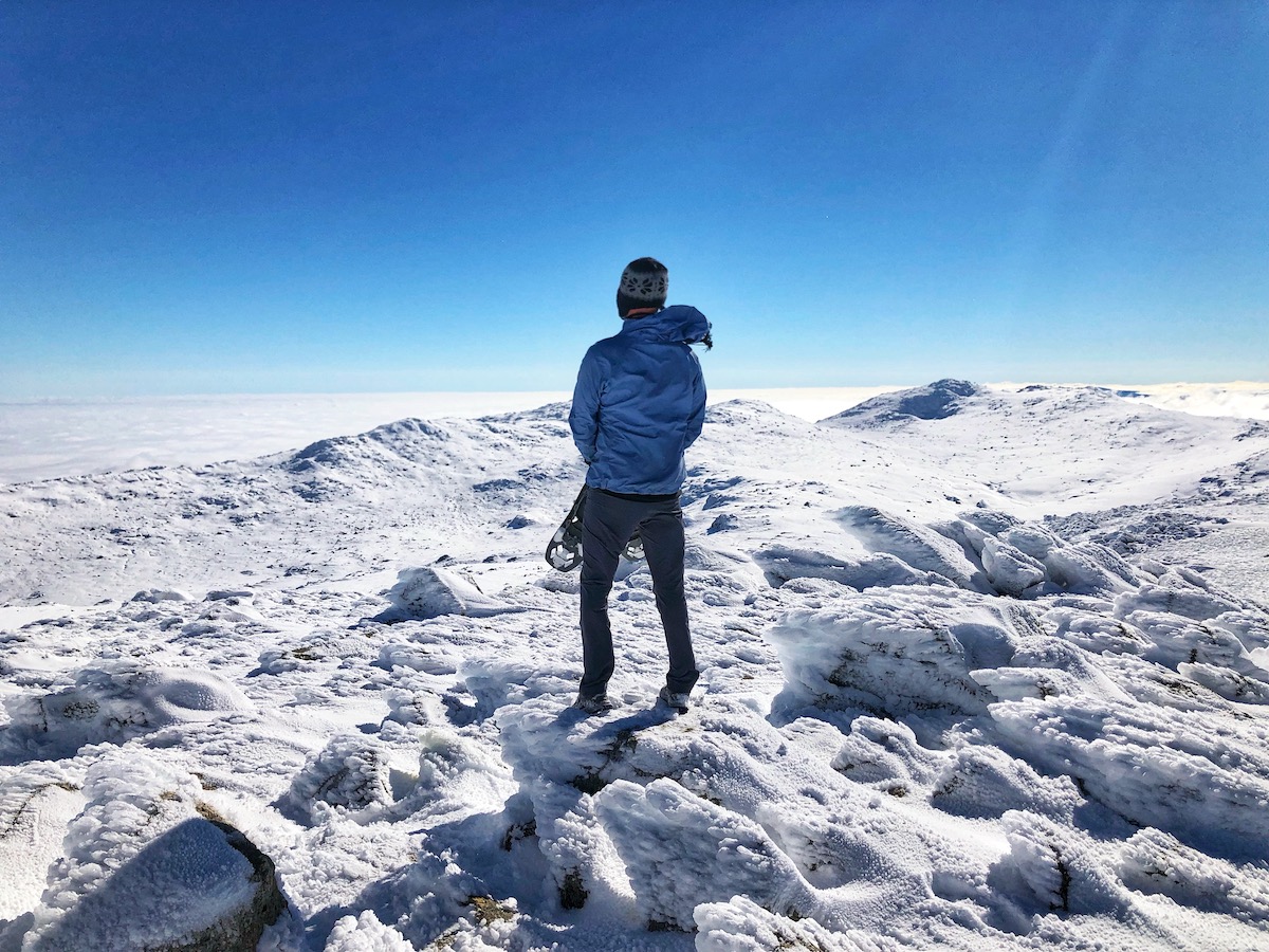 A man standing on top of a snowy mountain holding ski shoes.