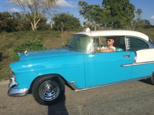 A man in a classic blue and white Chevrolet gets ready for a road trip in Cuba