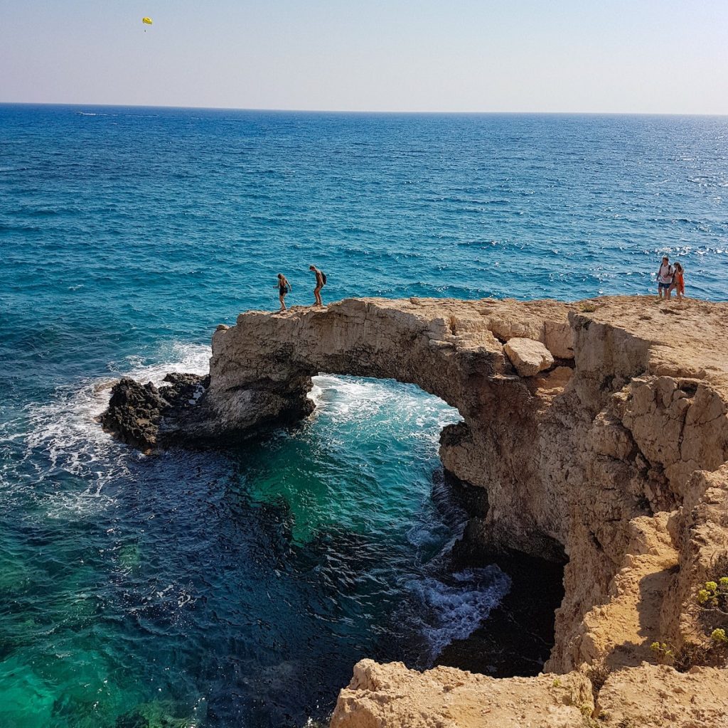 Couple of people standing on top of a cave in Cyprus, with a backdrop of Sea