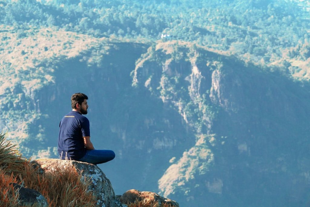 Man sitting on top of Adam's Peak in Sri Lanka, overlooking a beautiful view