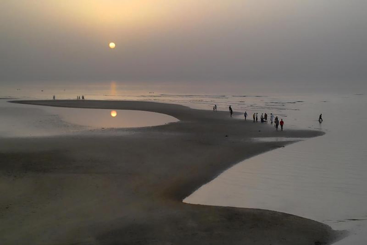 Sun sets over Qurum Beach as locals walk along the shore