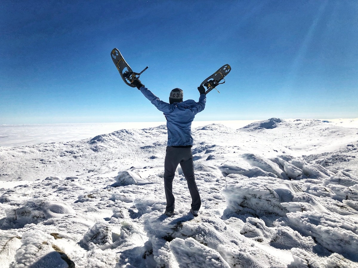 Hiker raises his snowshoes above his head on top of a snow-capped mountain in Australia