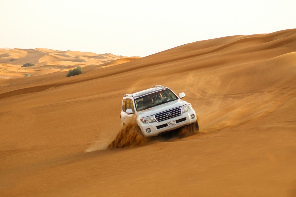 A white SUV leans to the side during dune bashing in the desert