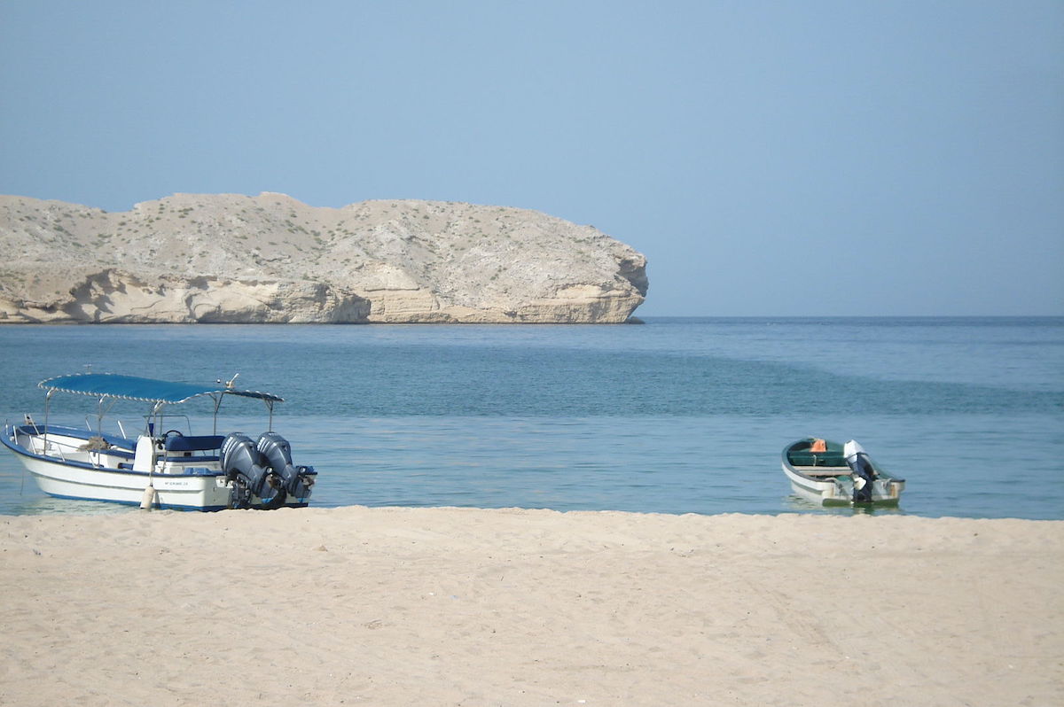 A medium and small-sized boat park up on a white sandy beach in Muscat, Oman.