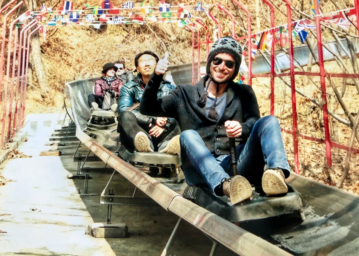 A man in a hat smiles at the bottom of a toboggan ride.