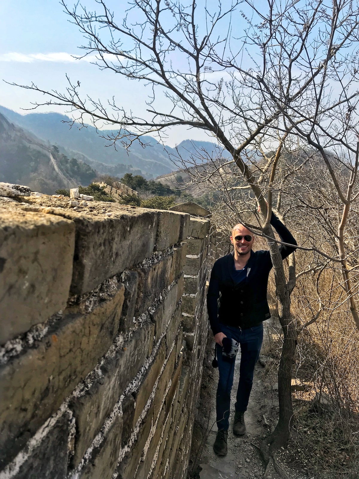 Male tourist with sunglasses smiles next to a tree in China.