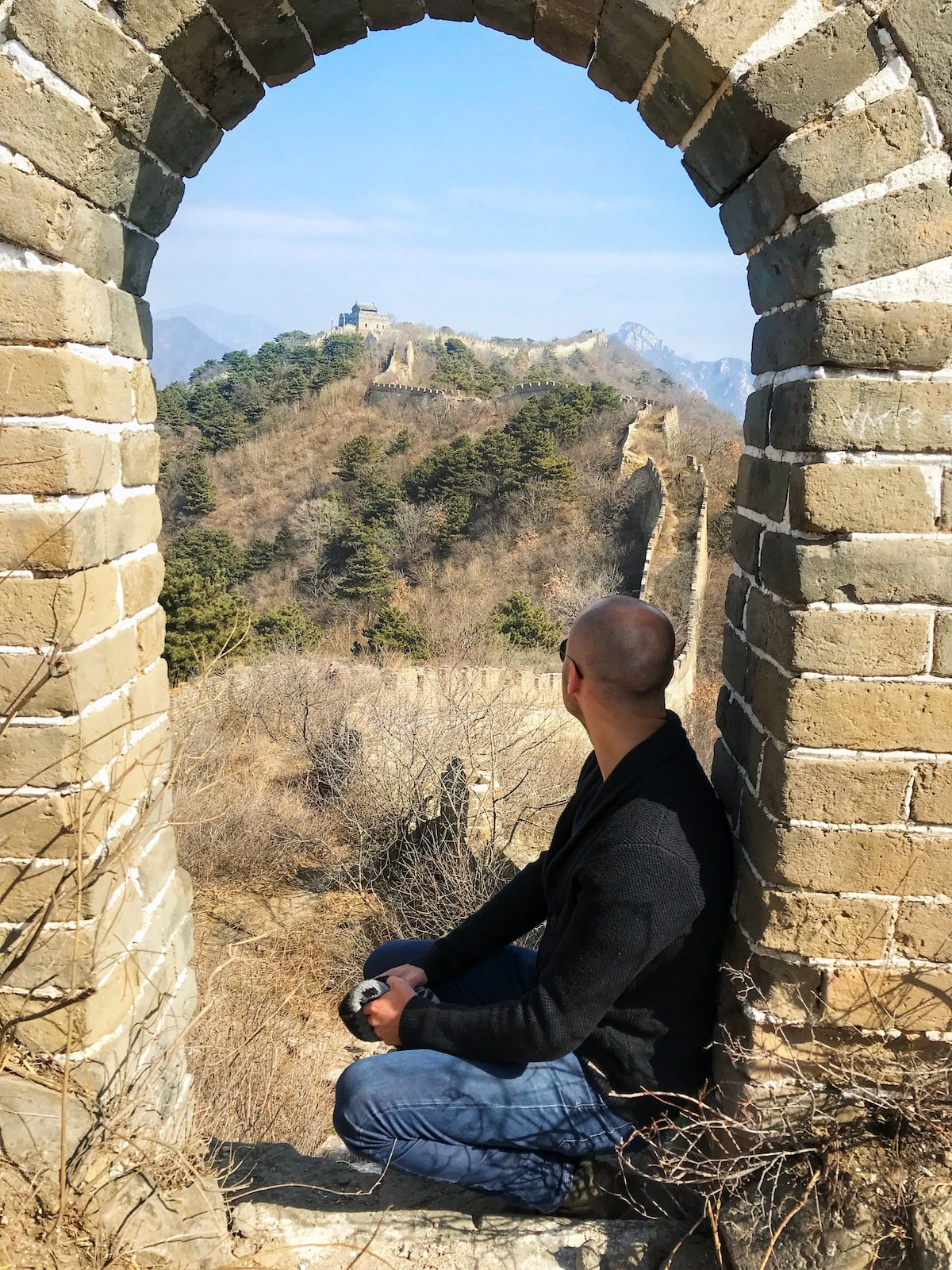 A male tourist looks out into The Great Wall of China from an archway on a sunny day in Beijing.
