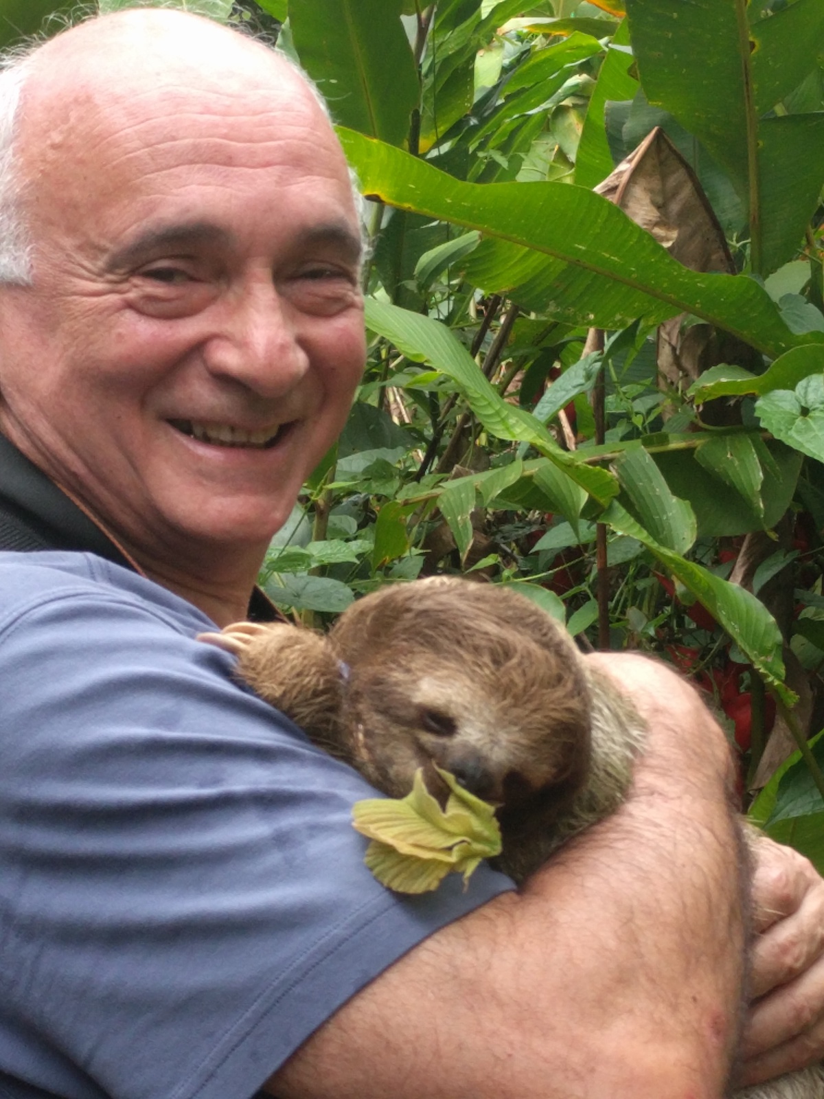 A middle-aged man smiles as he holds a baby sloth in Costa Rica.