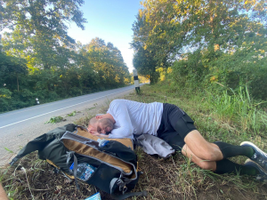Man in running gear takes a nap during an ultramarathon on the side of the road.