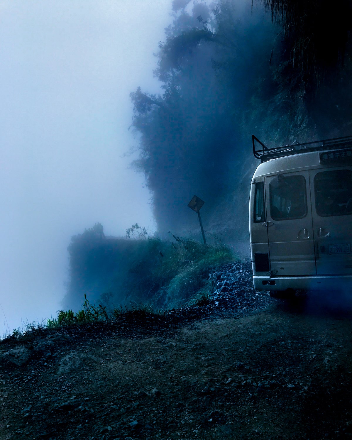 A van drives over a tight bend on a cliff with no barriers on Bolivia's Death Road.