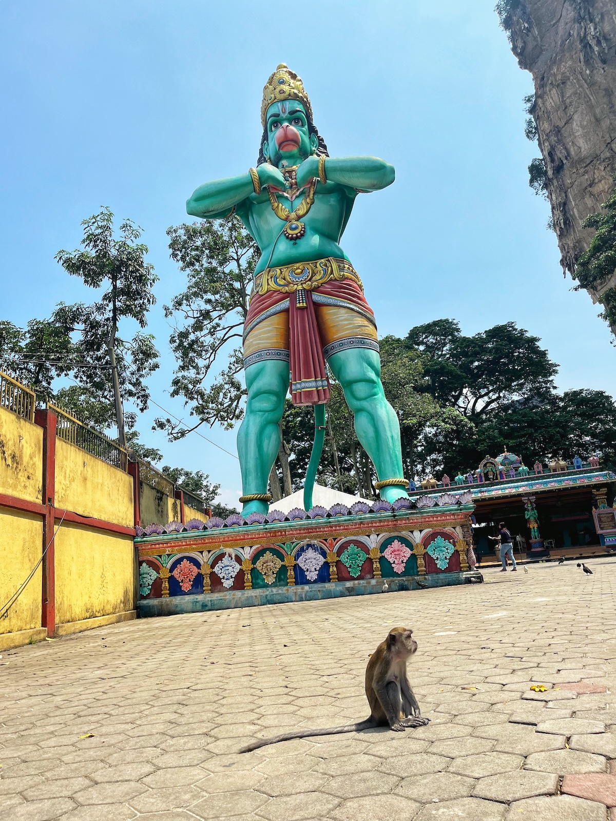 A small monkey looks onward below a giant statue of a Hindu monkey God in Kuala Lumpur