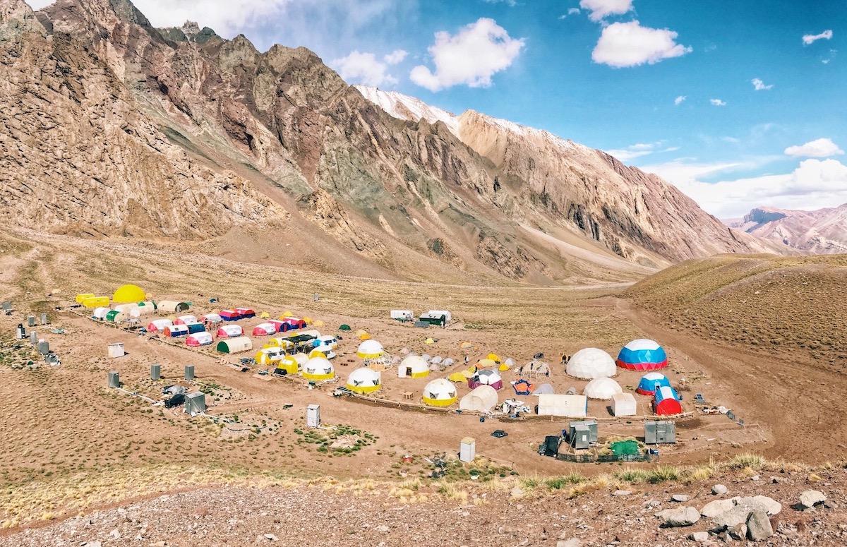 A sea of different coloured tents stand out on a large brown landscape of a mountain at Camp Confluencia on Aconcagua 