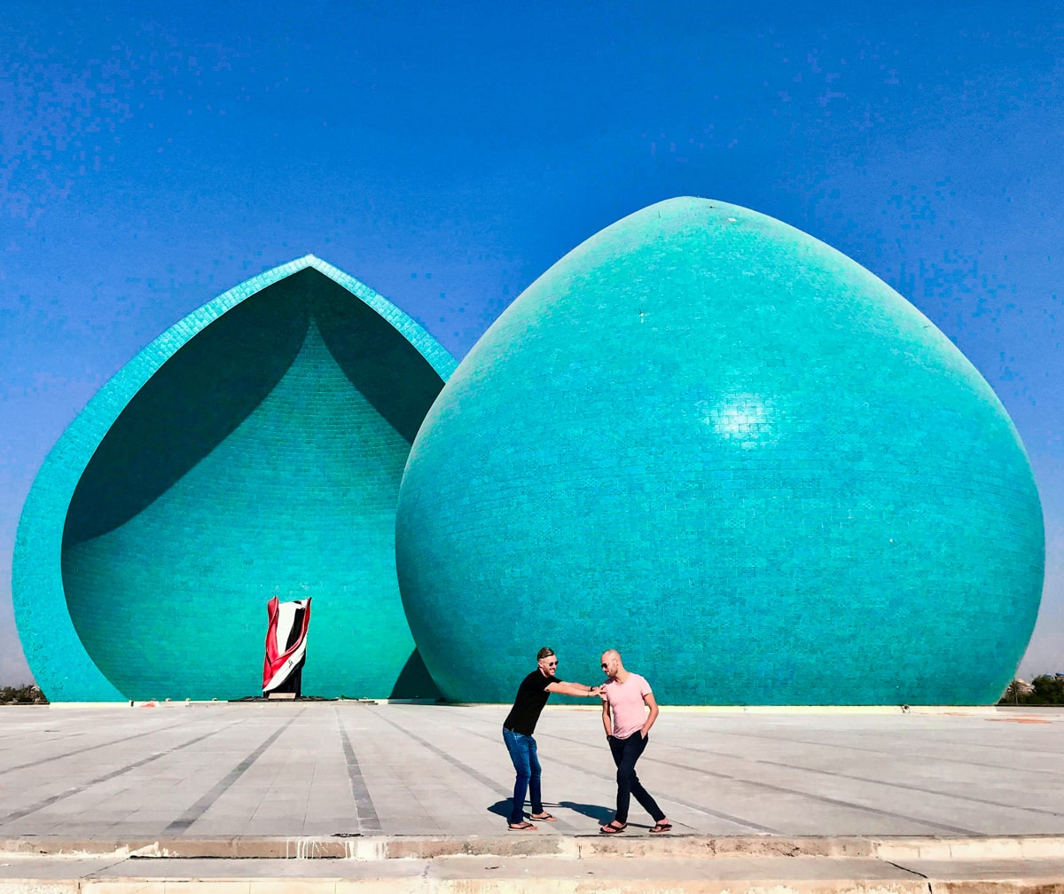 Two male tourists stand near the green dome of Al Shaheed Martyrs Monument while visiting Baghdad 