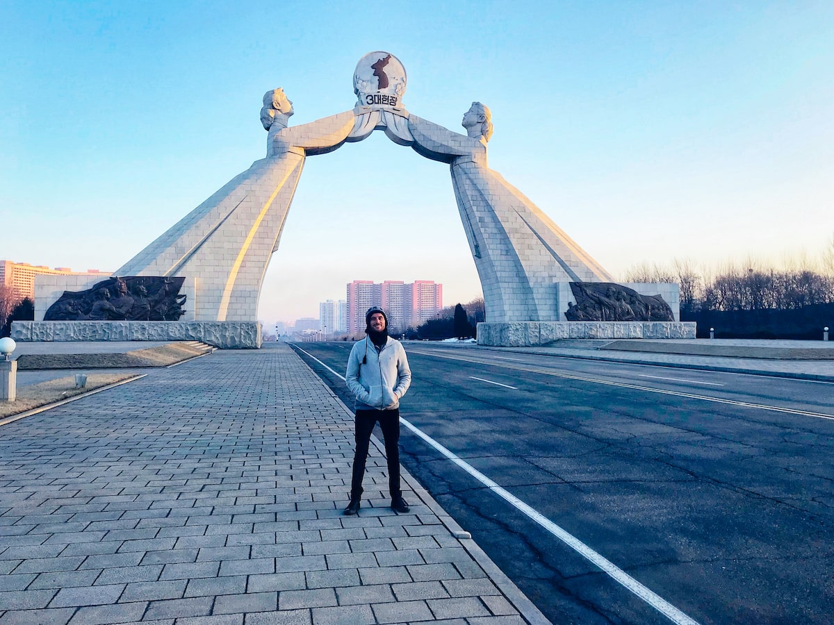 A male tourist stands in front of the Arch of Reunification monument in North Korea