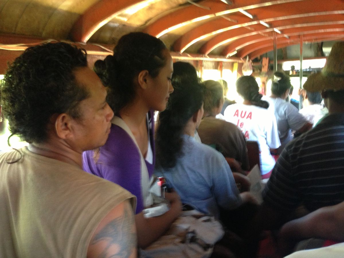 A young lady sits on a man's knee on a crowded bus in Samoa.