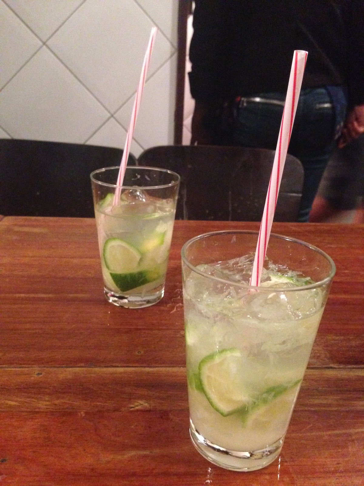 Two caipirinhas with lime on a wooden table.