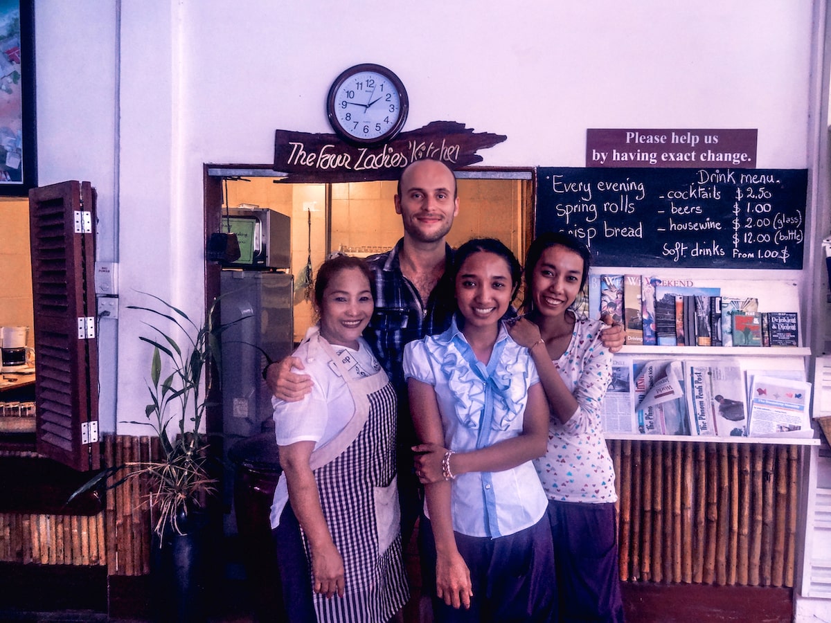 A male tourist poses with 3 Cambodian ladies in a restaurant. 