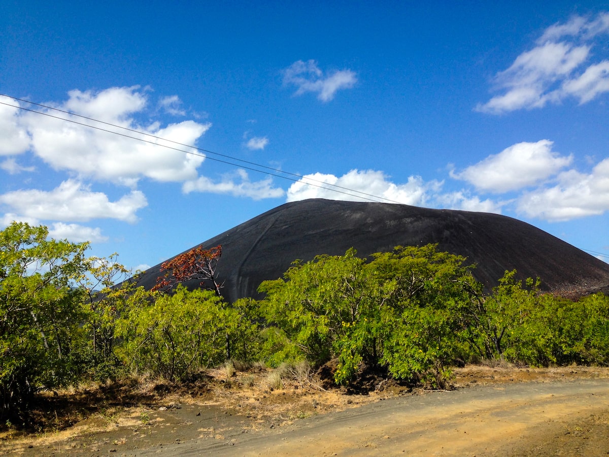 A volcano on a clear blue sky day with green trees outside of it. 