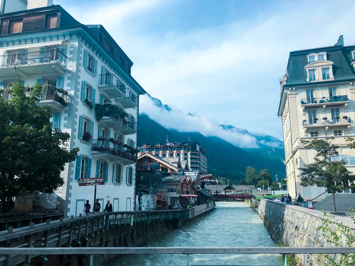 A bed of water flows through a pretty citym misty clouds drift over nearby mountains,