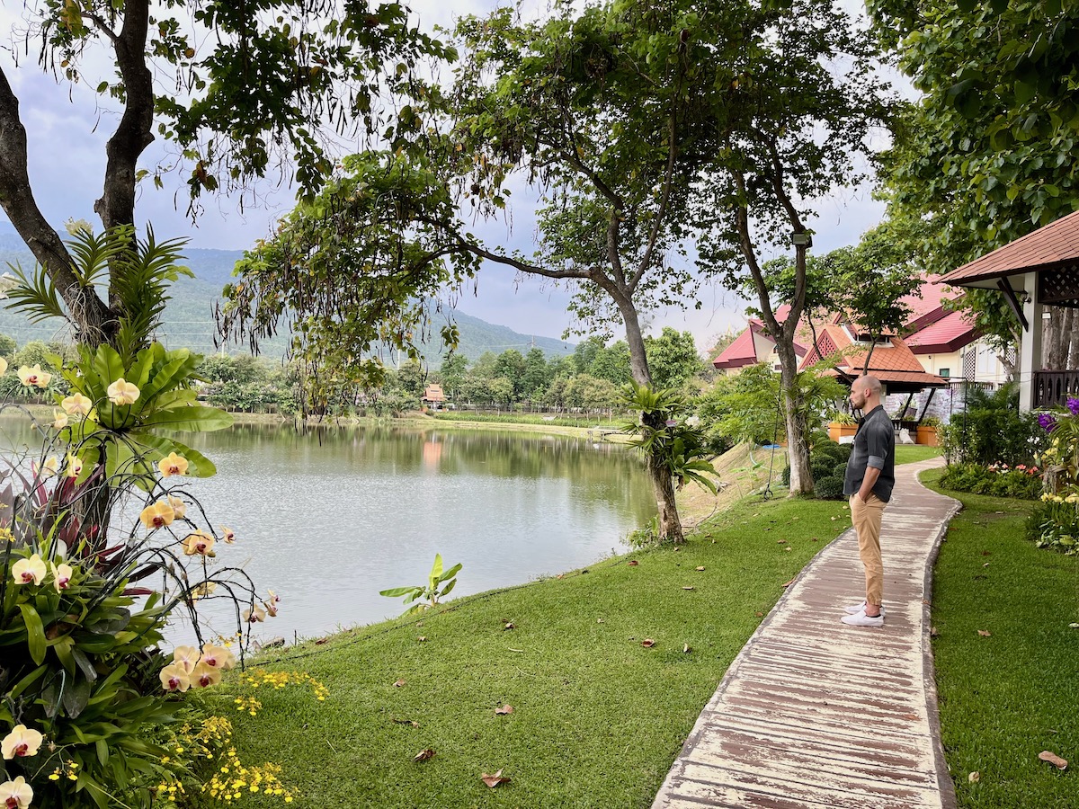 A man in a black shirt looks out into a beautiful view of a lake and trees surrounding a green mountain in Chiang Mai, Thailand