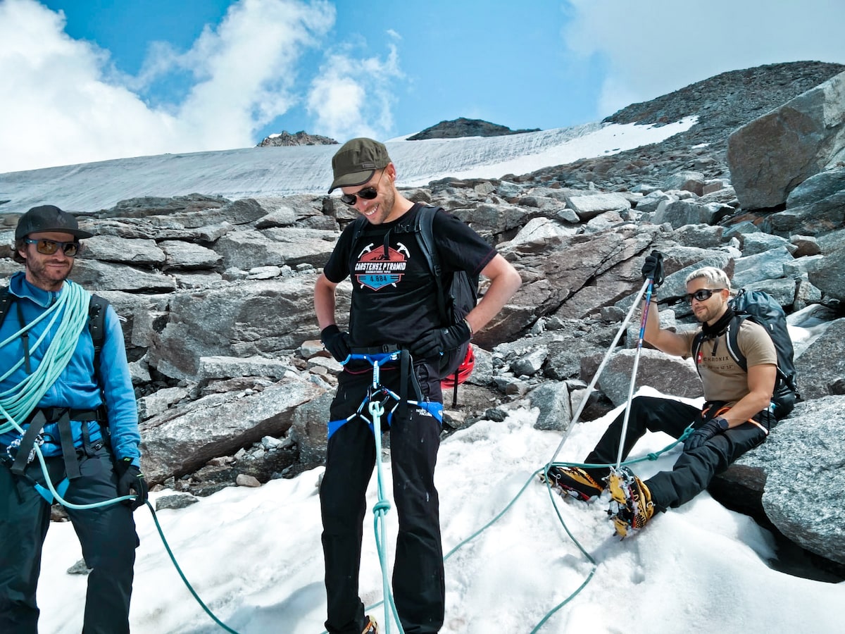 Three mountain climbing men pause for a smile as they rope themselves together.