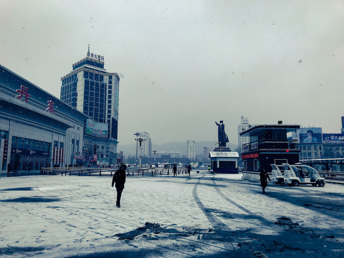 Locals walk the cold streets of Dandong in China with snow falling on the ground