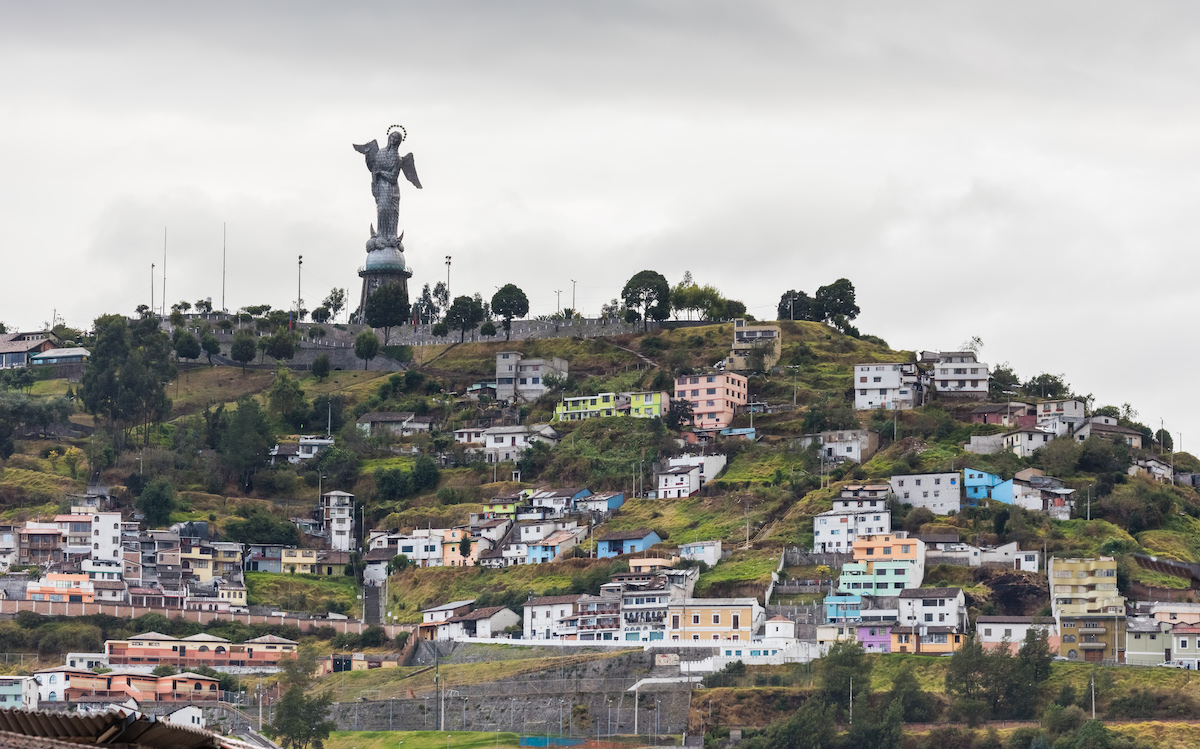 A statue of The Virgin Mary on top of a hill with coloured houses surrounding Quito, Ecuador. 
