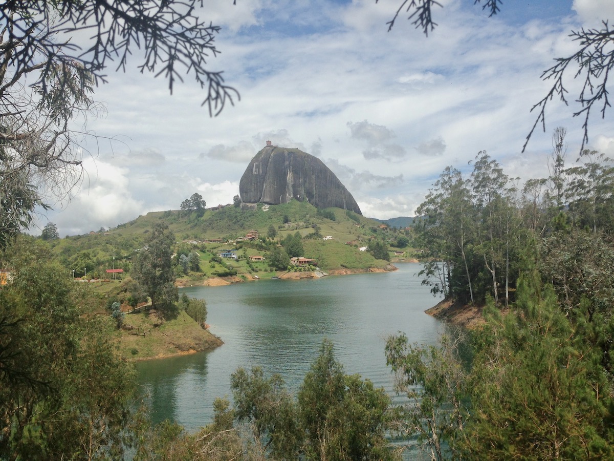 A giant rock towers above a green valley on a bed of water in El Peñol, Colombia