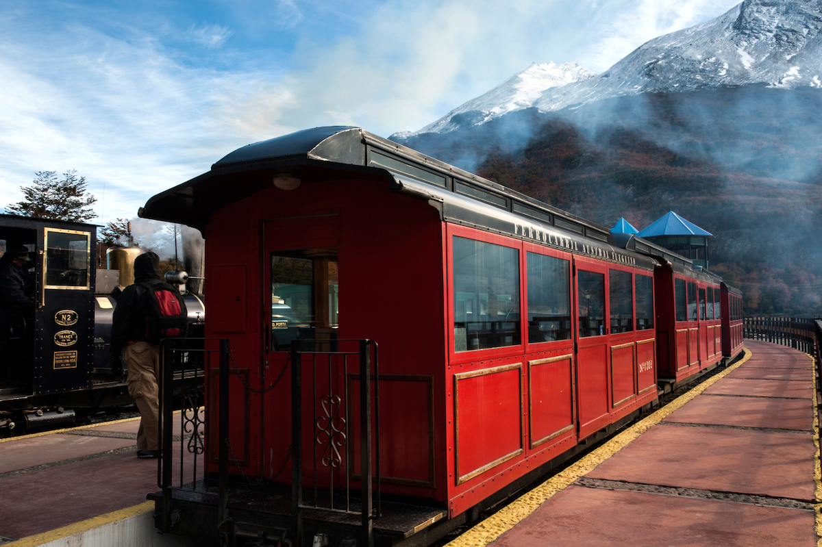 A red tram stops alongside a snow-capped mountain in Tierra del Fuego, Ushuaia, Argentina 