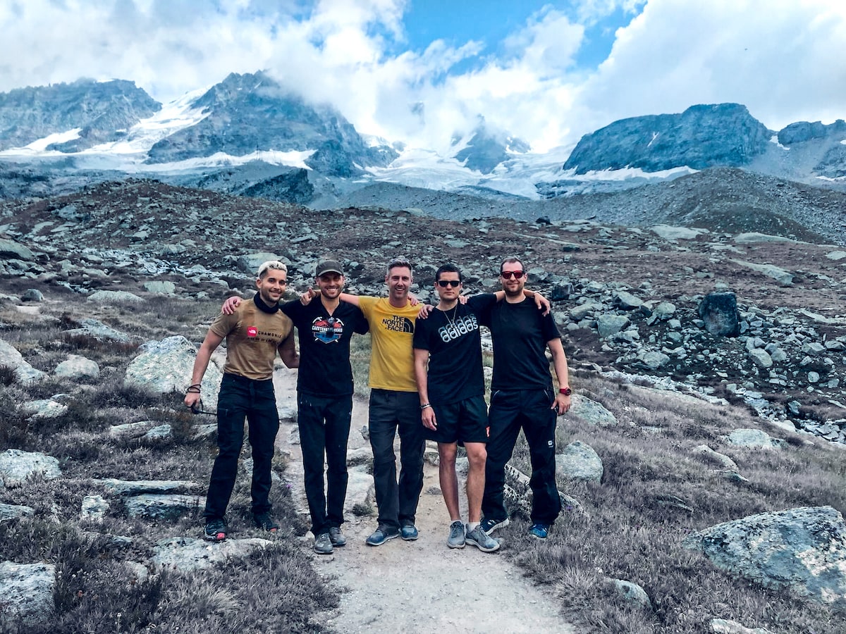 Five men with arms on each other's shoulders pose in the French Alps in front of icy, snow-capped mountains.
