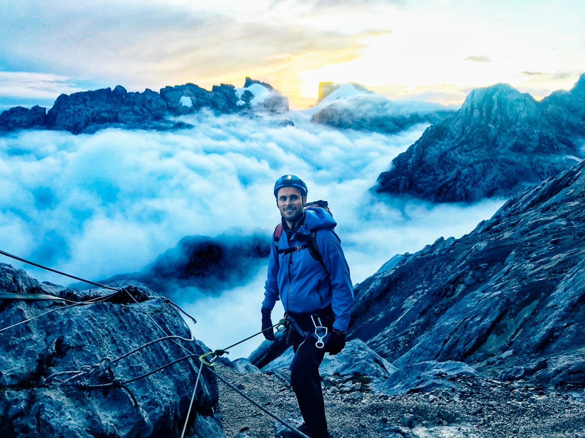 A climber in blue standing above the clouds while climbing Puncak Jaya
