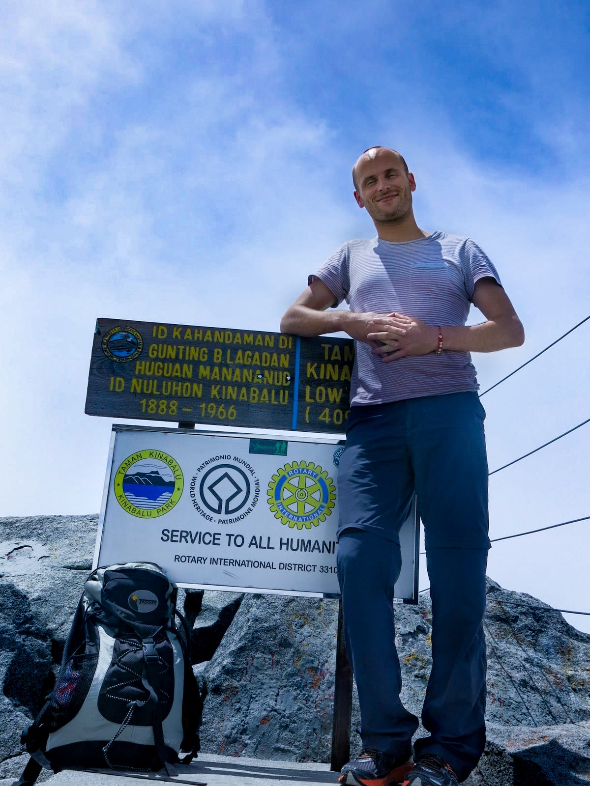 A man smiles as he leans on a sign with Bahasar writing on the summit of Mount Kinabalu, in Malaysian Borneo. 