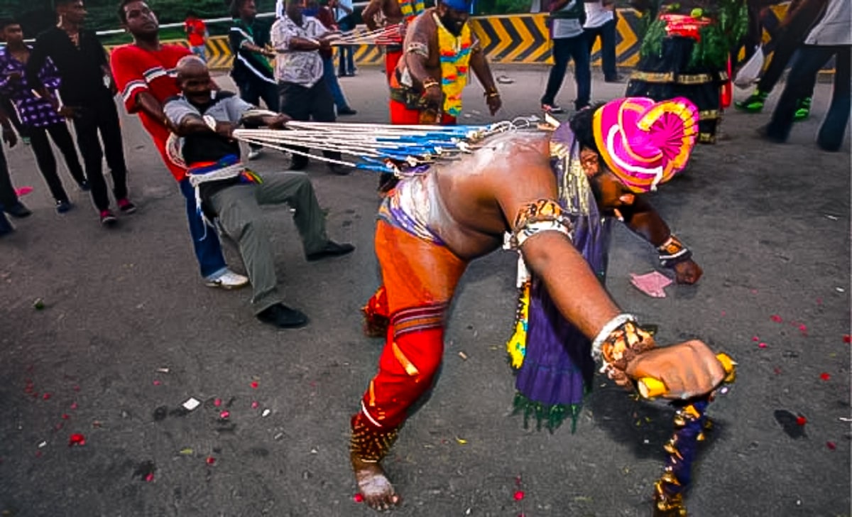 Two men hold back a man on a metal leash that is attached to his body at the Hindu Thaipusam Festival in Batu Caves, Kuala Lumpur