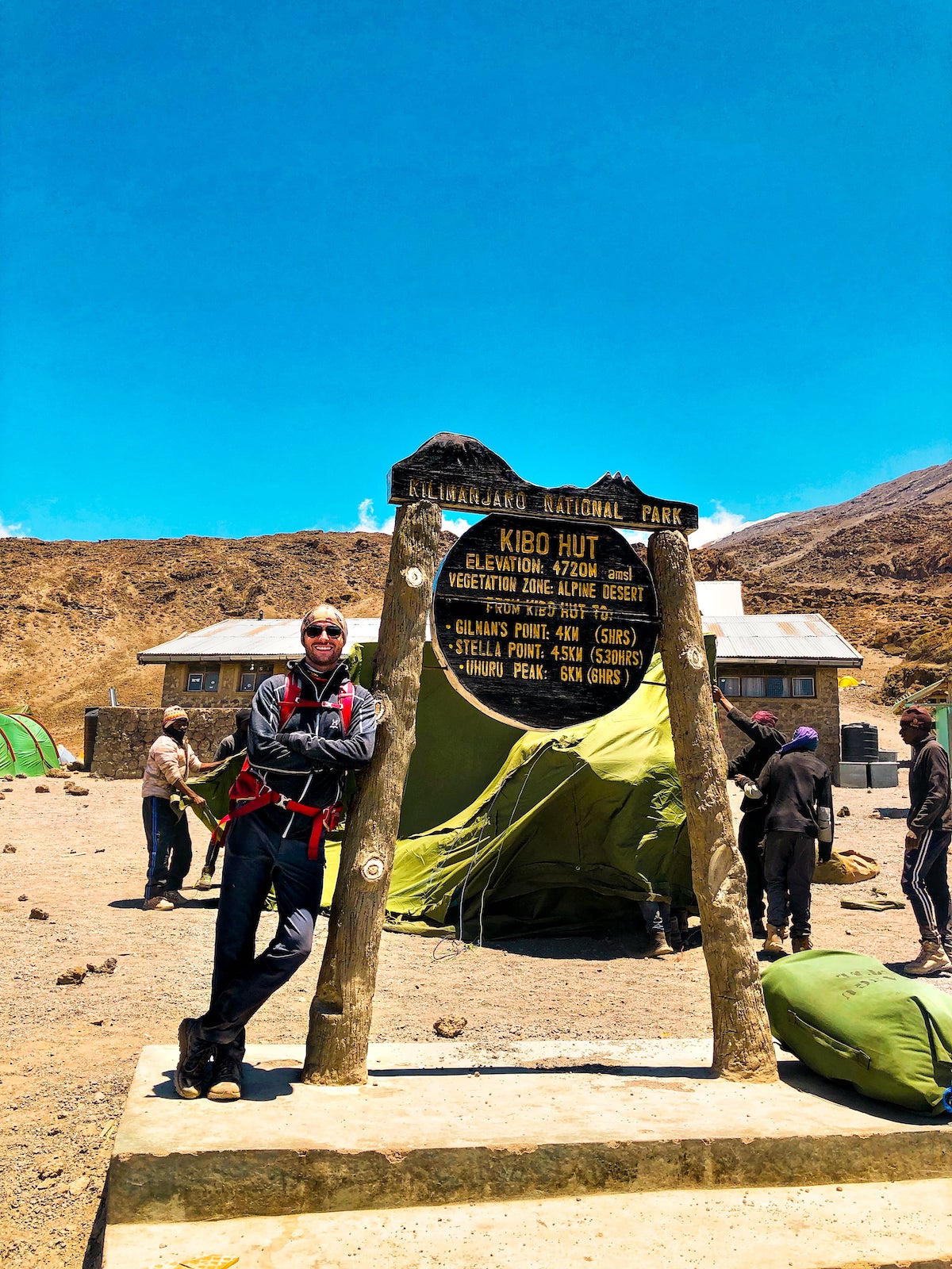 A male hiker confidently leans against a signpost in Kilimanjaro National Park.