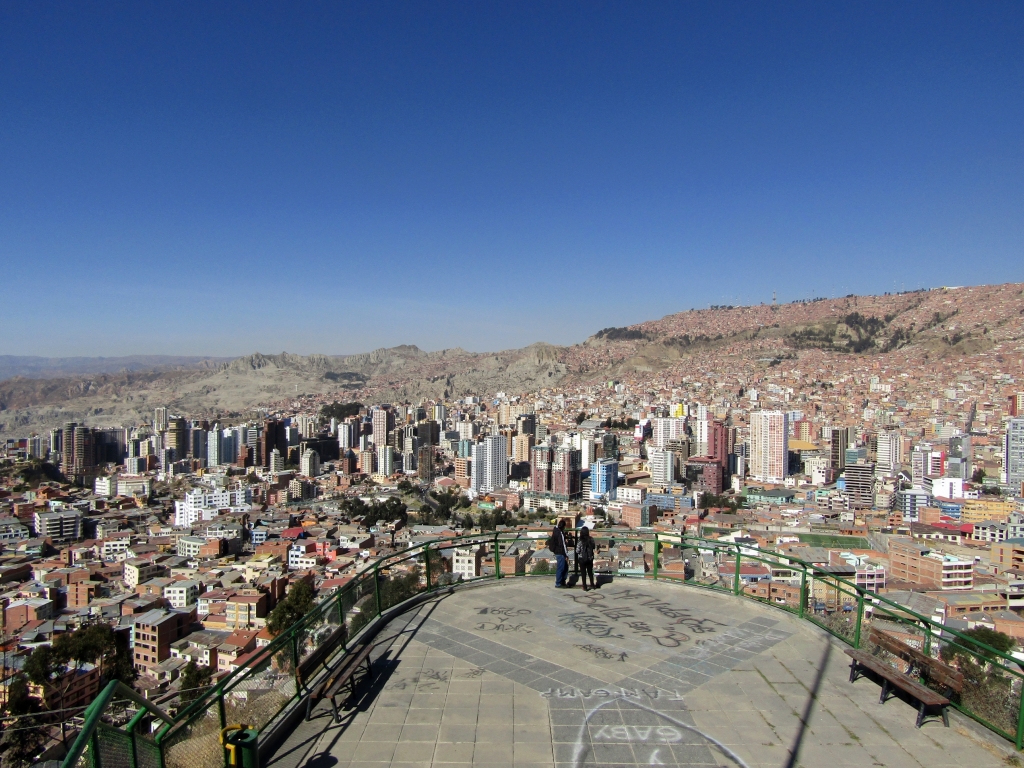 A viewpoint overlooks a busy city of in front of a moon-like backdrop during the day in La Paz, Bolivia
