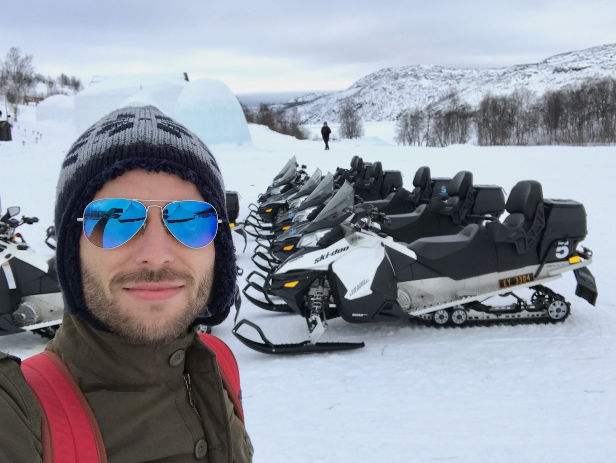 A man poses next to snowmobiles parked on a snowy landscape in Kirkenes, Norway.