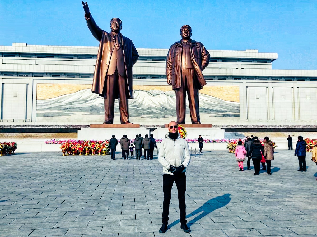 A male tourist poses in front of two large bronze statues of Kim Il-sung and Kim Jong-il during a North Korea travel experience at Manu Grand Hill Statues