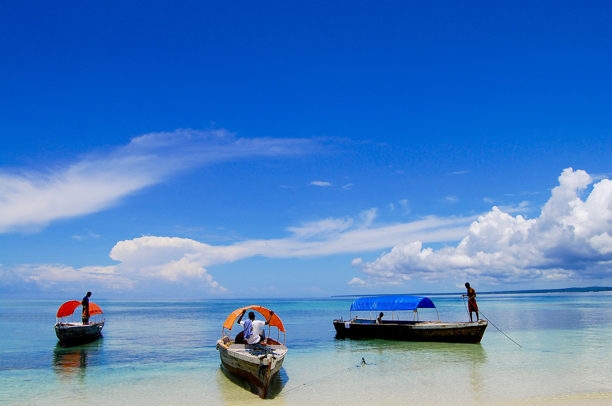 Three colourful boats on the shore of a beautiful clear blue sea