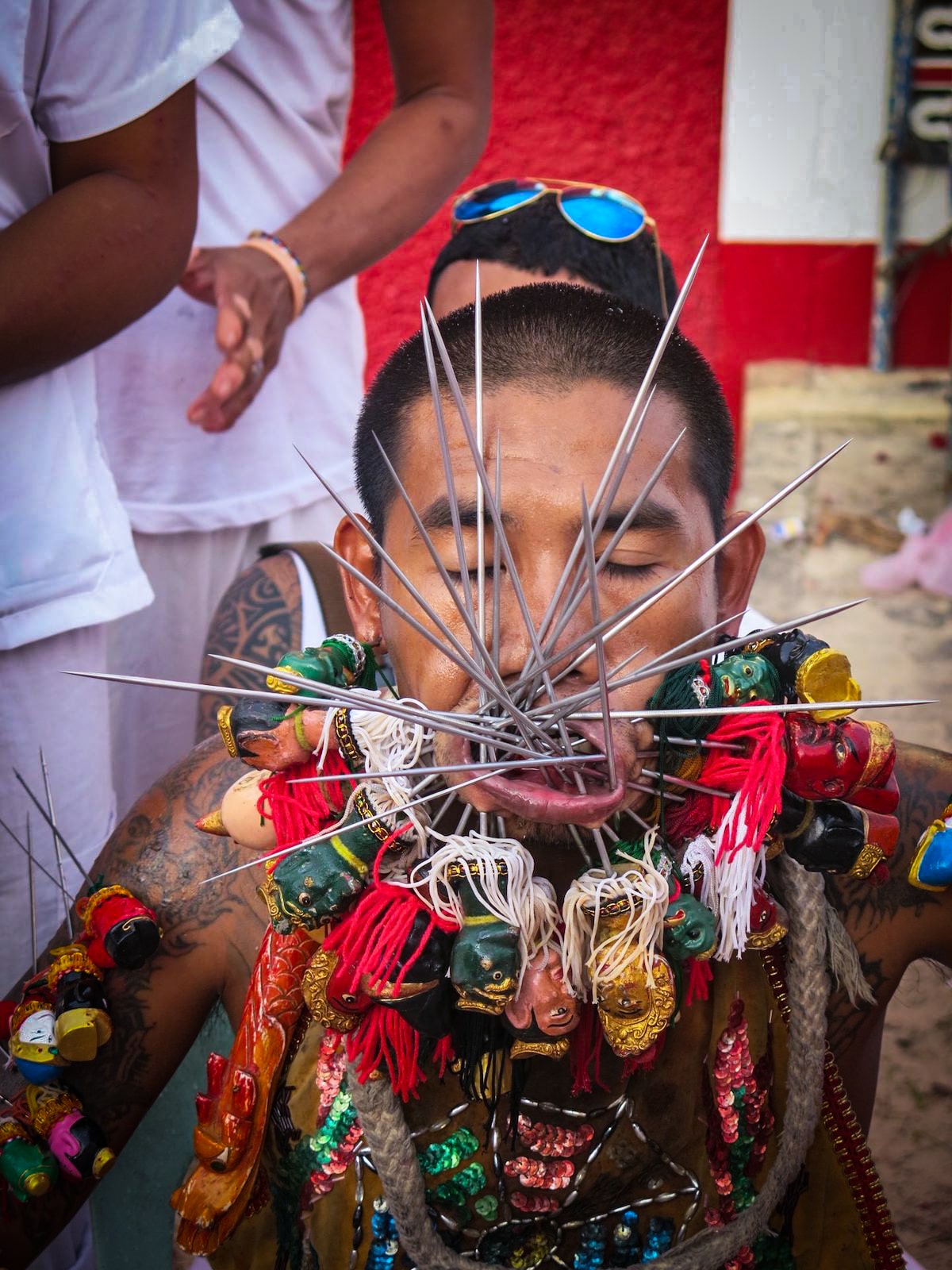 A man with several needles through his face, adorned with colourful tribal ornaments. 