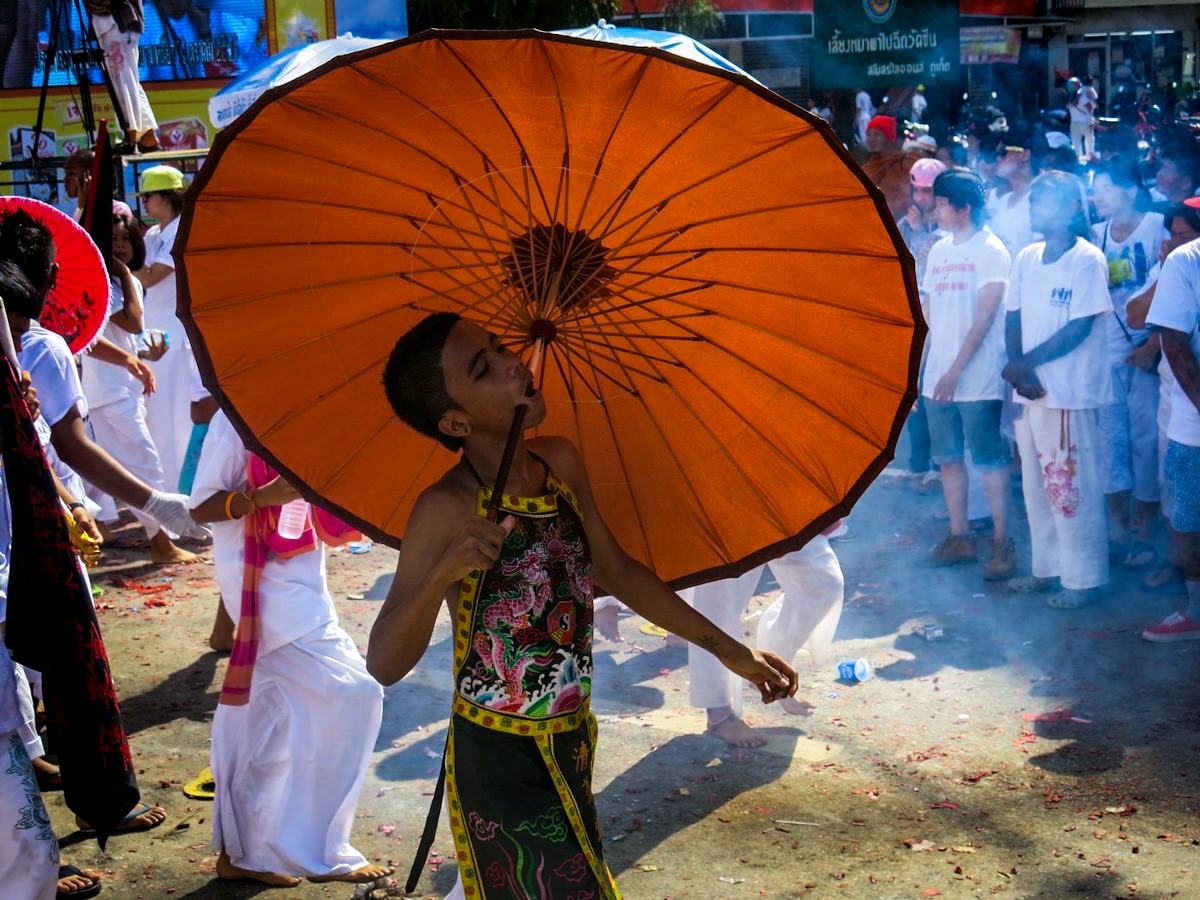 A boy walks with an umbrella pierced through his cheeks at the Phuket Vegetarian Festival. 