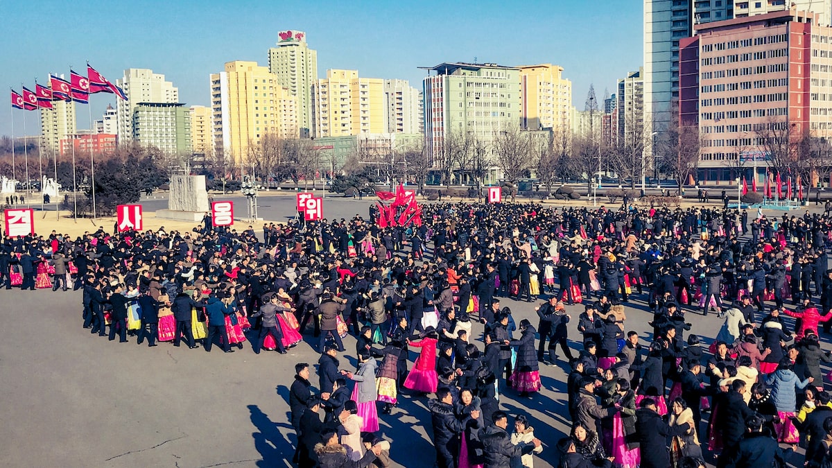 Thousands of people dance together in the streets of Pyongyang in front of North Korea flags.