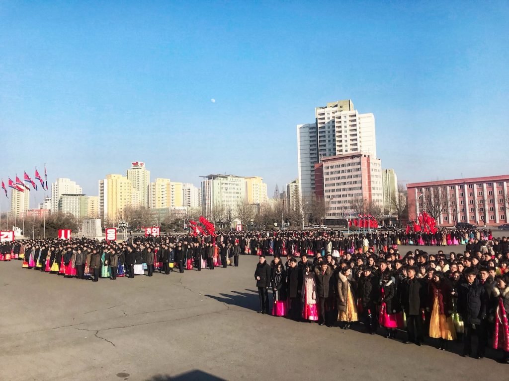 Masses of people in traditional clothing line up in a uniformed manner in a public square in North Korea