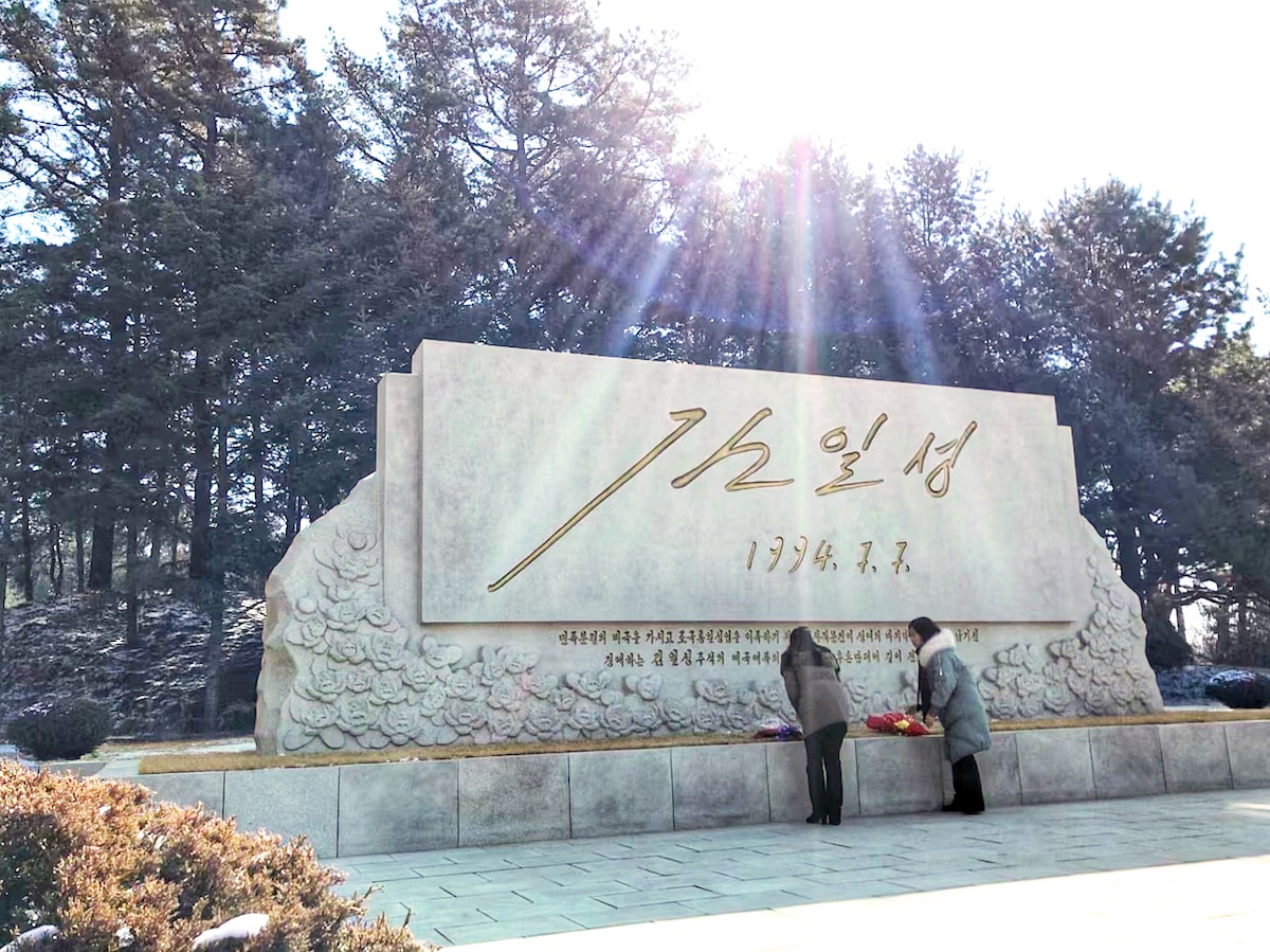 Two North Korean ladies lay down flowers in front of a monument in North Korea at the DMZ border